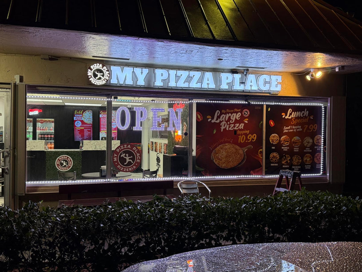 Illuminated storefront signs and window graphics at a pizza restaurant at night