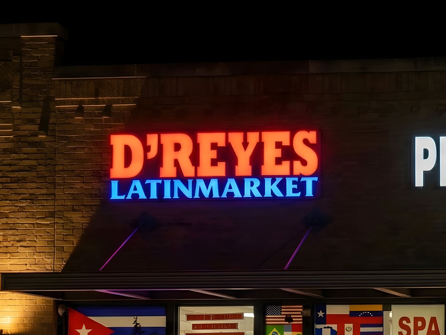 Face-lit channel letter sign for D’Reyes Latin Market, mounted on a brick storefront and glowing at night