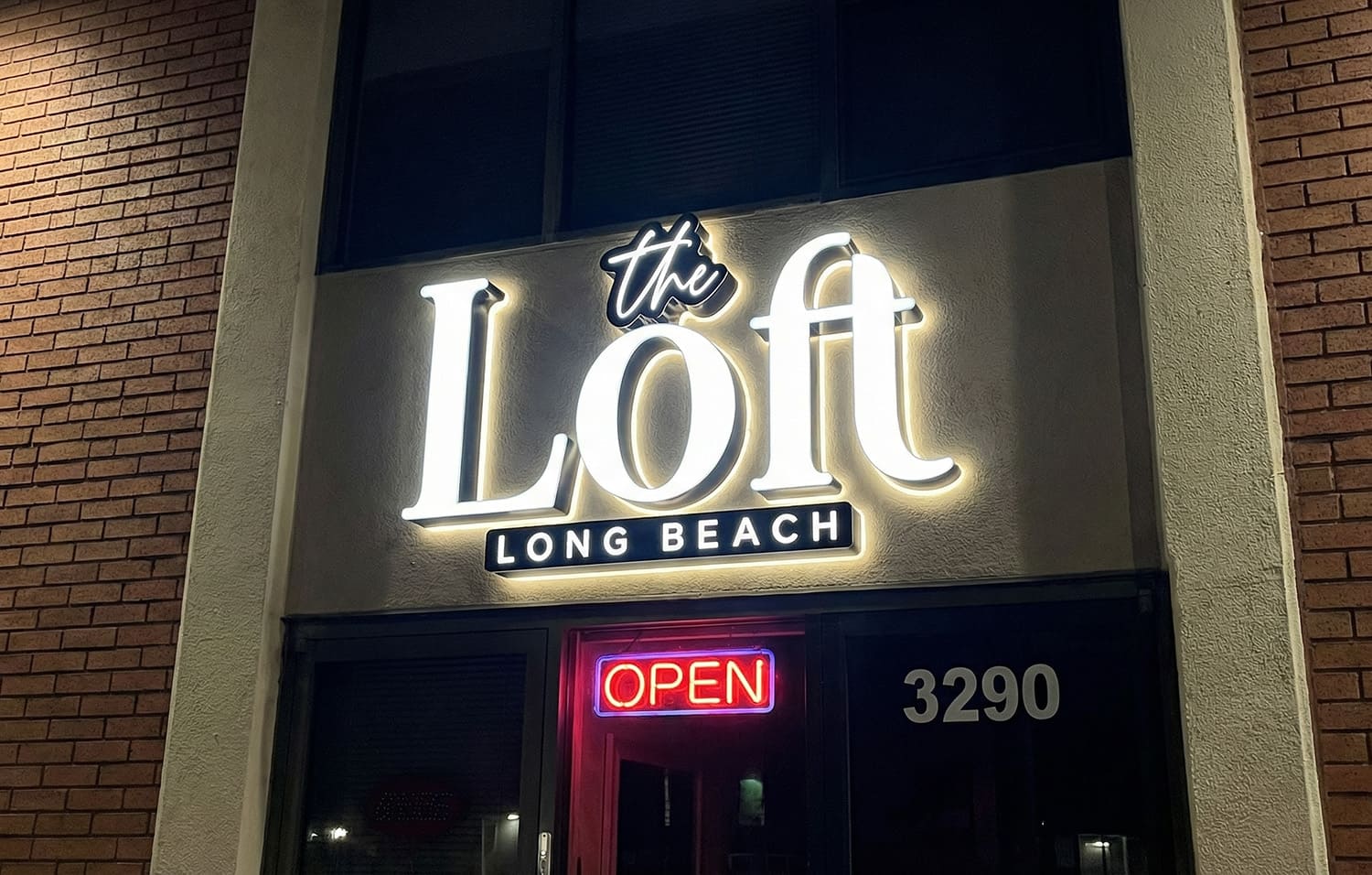 The Loft Long Beach halo-lit sign glowing at night above the entry door